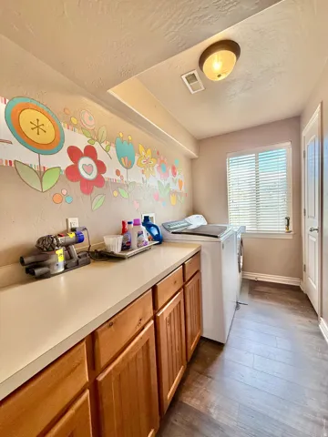 Wood-finish flooring, built-in wooden cabinetry, light-toned countertop, and window with blinds