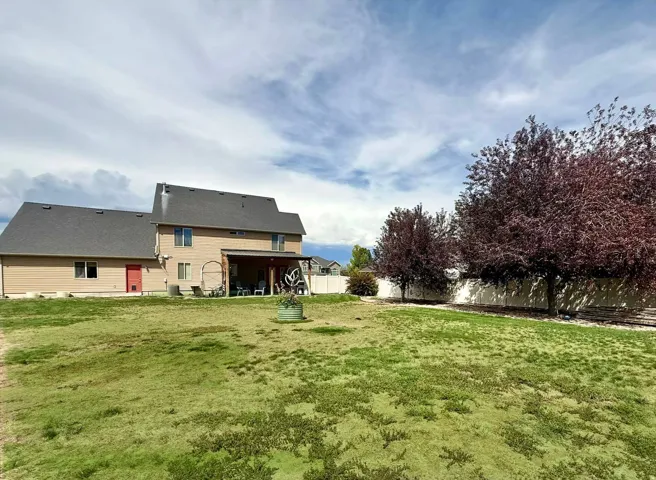 Expansive backyard featuring a covered patio, multiple shade trees, and a privacy fence