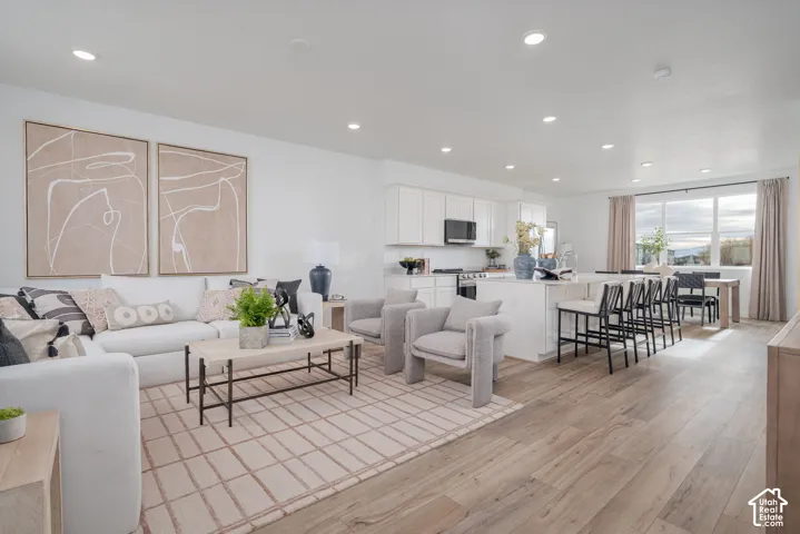 Open-concept living area with wood-finish flooring, recessed lighting, and a white kitchen with an island