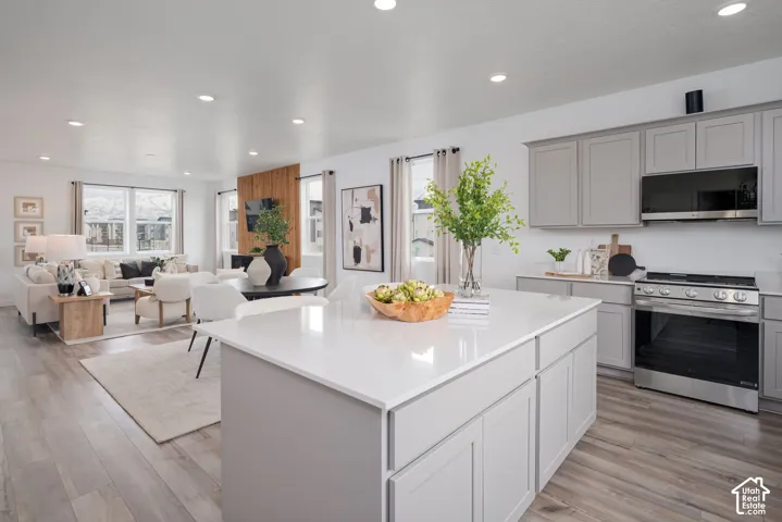 Open concept living area featuring light wood-finish flooring, recessed lighting, a kitchen island with a light countertop, and light gray cabinetry