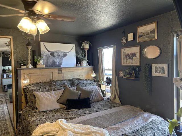 Recessed window with drapes, mounted wall art, ceiling fan with integrated lighting, and a built-in wooden headboard