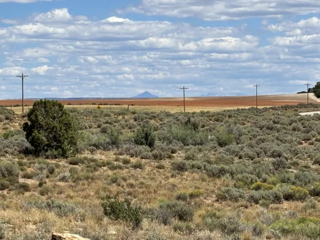 Expansive rural landscape featuring natural brush, distant mountains, and a clear sky with scattered clouds