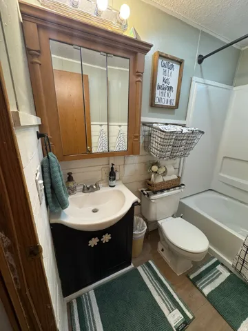 Enclosed bathroom featuring a white porcelain toilet, a white porcelain tub with shower kit, a black vanity with a white ceramic sink, and a wood-finish medicine cabinet with mirrored doors