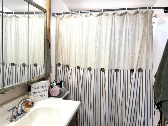 Vanity with an integrated sink and chrome faucet, framed mirror, and a shower with a two-toned curtain