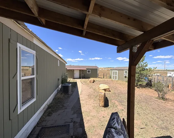Covered patio with exposed wood beams, a paved walkway, and a detached structure with a metal roof