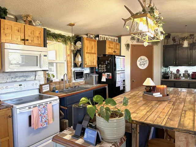 Kitchen featuring wood-finish cabinetry, built-in microwave, stainless steel sink, black-finish refrigerator, and a large central island with a wood-plank surface