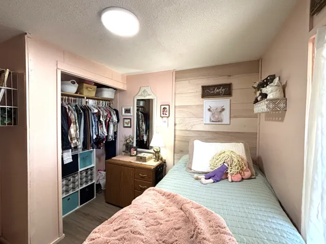 Recessed ceiling lighting, wood-finish flooring, built-in closet with shelving, wood panel accent wall, and a framed mirror