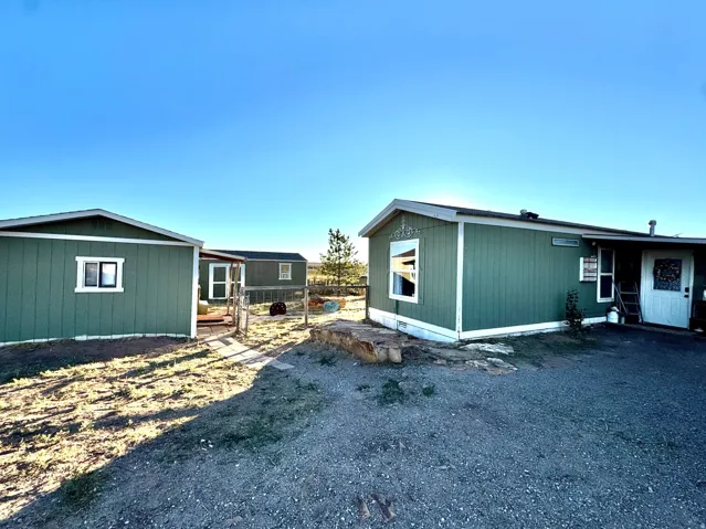 Green exterior siding with white trim, multiple structures, and a gravel driveway