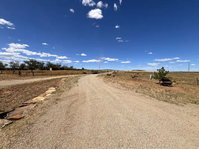 Gravel driveway with natural stone border, expansive open land, and scattered trees