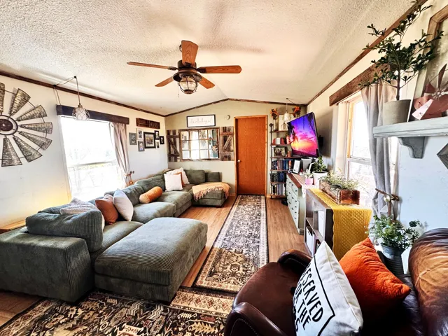 Wood-finish flooring, ceiling fan with integrated lighting, exposed wood beam accents, and multiple windows