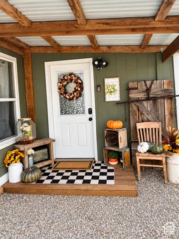 Covered porch featuring a corrugated metal roof, exposed wood beams, wood paneling, and a white entry door with privacy glass