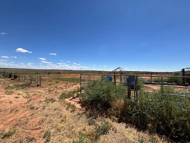 Expansive open land featuring a metal fence, arid ground cover, and a clear sky