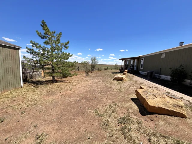 Expansive outdoor space featuring a covered porch, detached storage building, and natural landscaping with mature trees and large rock accents