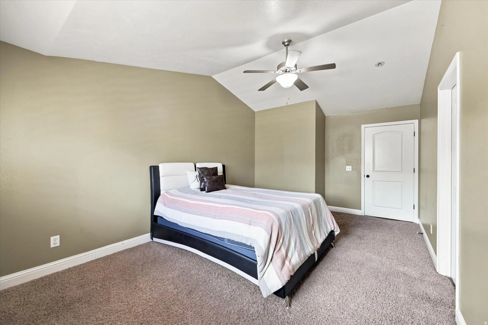Vaulted ceiling with a ceiling fan, neutral carpet flooring, and a paneled interior door