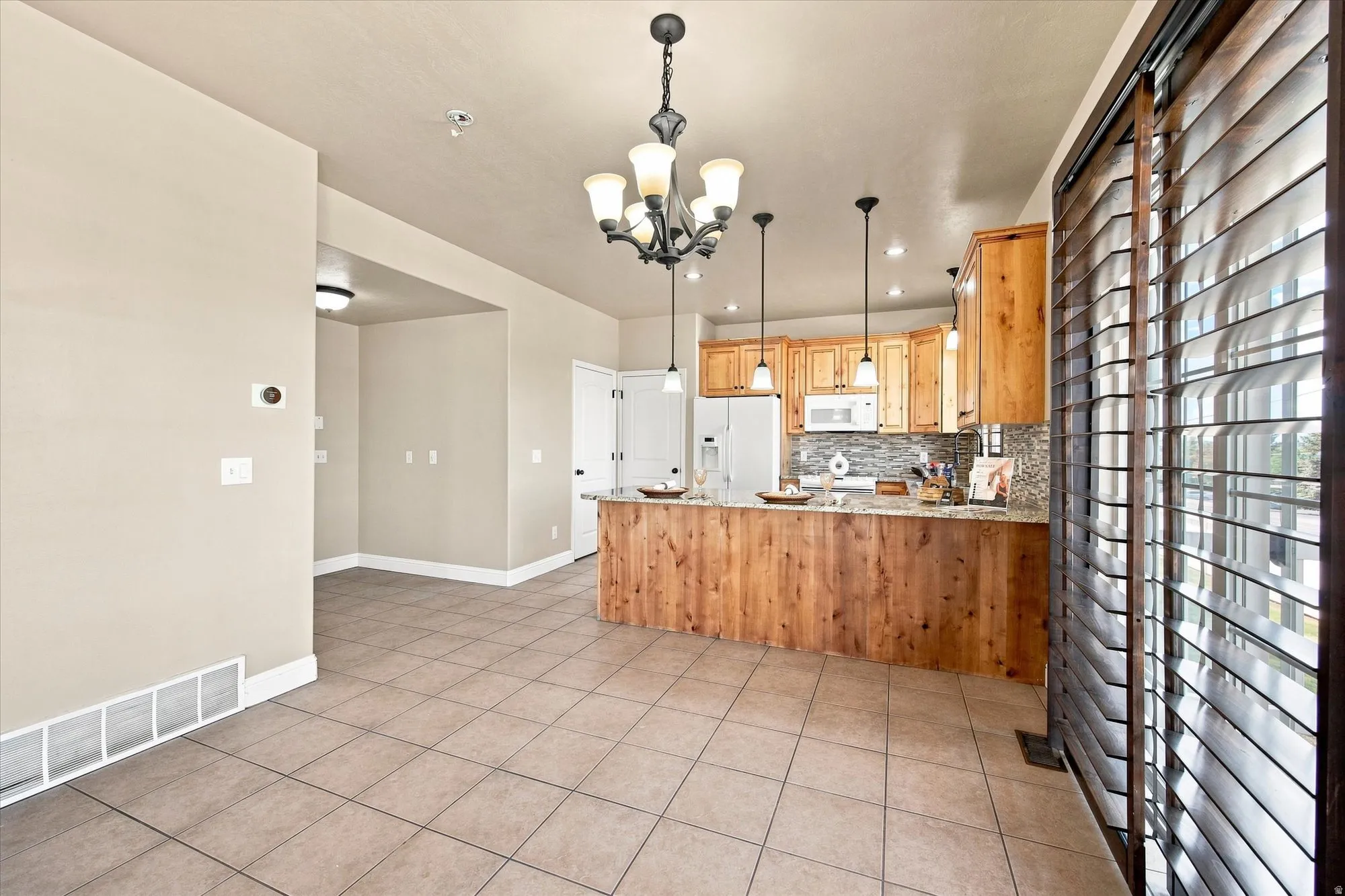 Kitchen featuring wood cabinetry, stone countertops, pendant lighting, and a tile backsplash