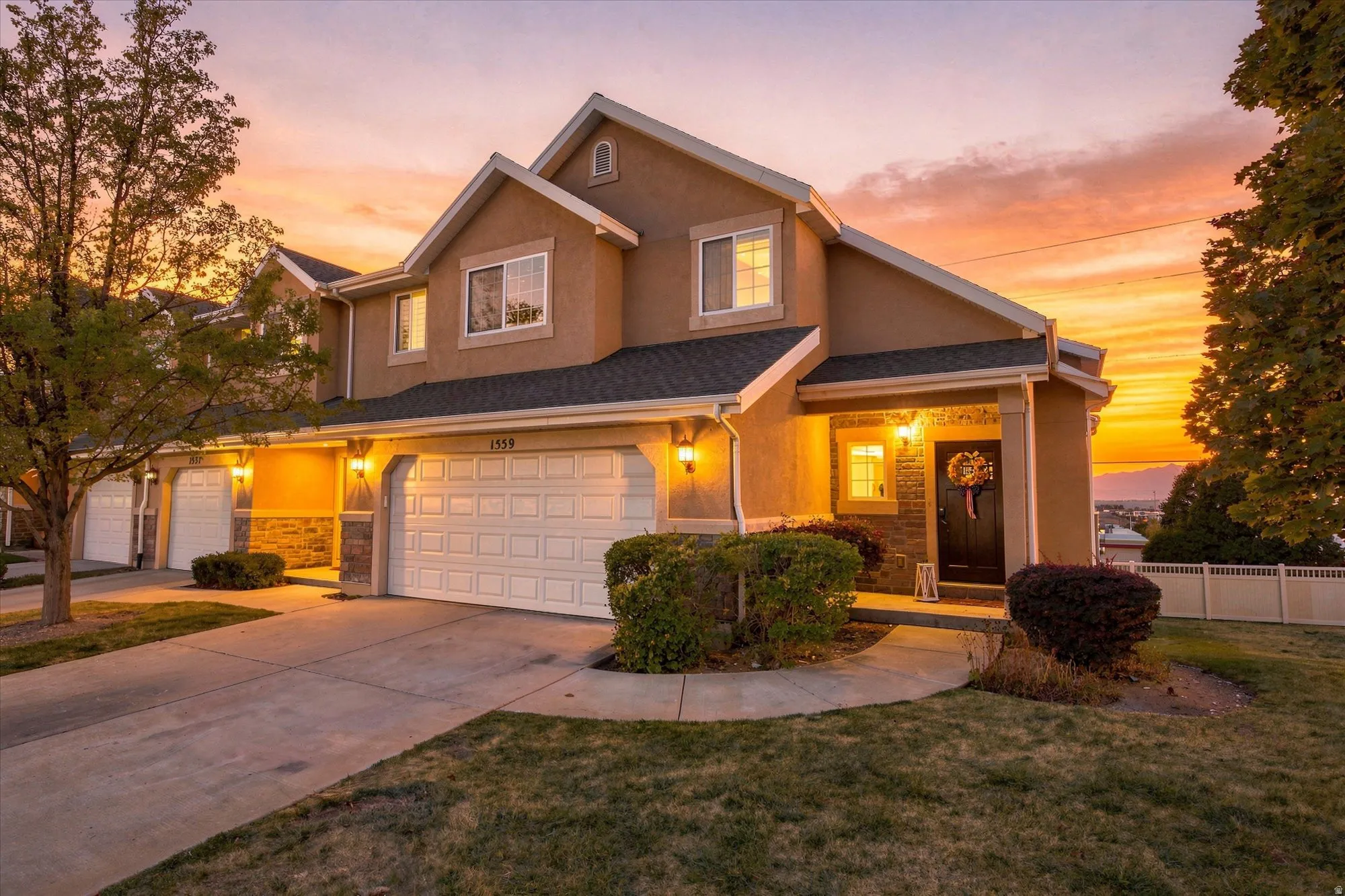 Stucco exterior with stone accents, attached two-car garage, covered front entry, and multiple exterior wall sconces