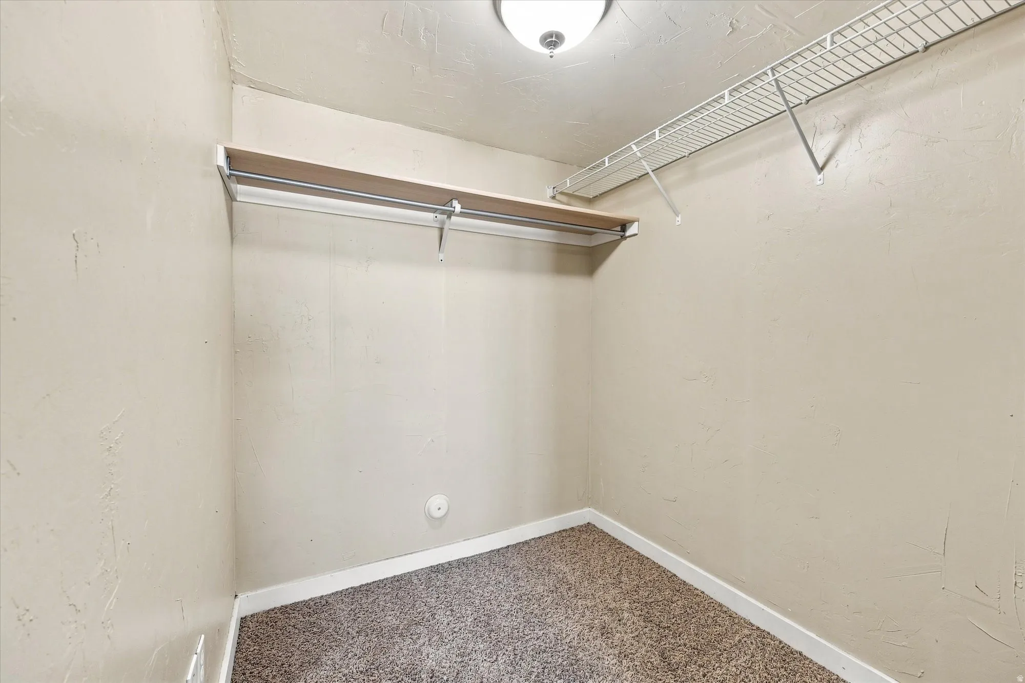 Built-in closet shelving, metal hanging rod, wire shelving, textured walls, and carpet flooring
