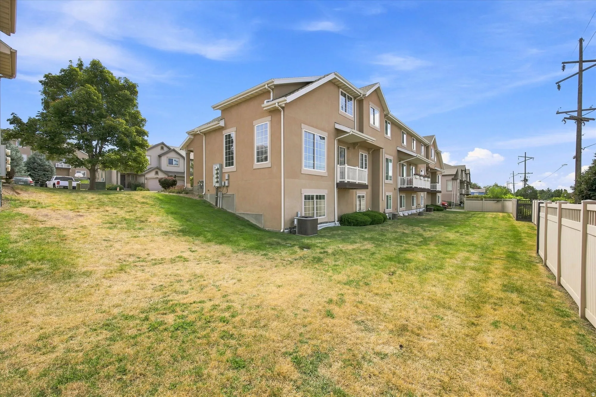 Multi-story stucco exterior with multiple balconies and white railings, featuring a fenced yard