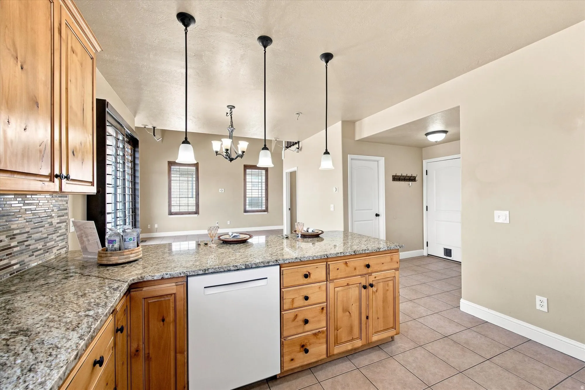 Spacious kitchen featuring custom wood cabinetry with multiple drawers, granite countertops, stainless steel appliances including a dishwasher, and a large island with seating