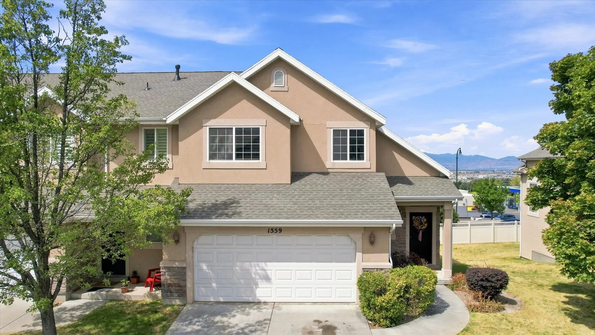Two-story stucco exterior with stone accents, attached two-car garage, covered porch entry, and mature landscaping