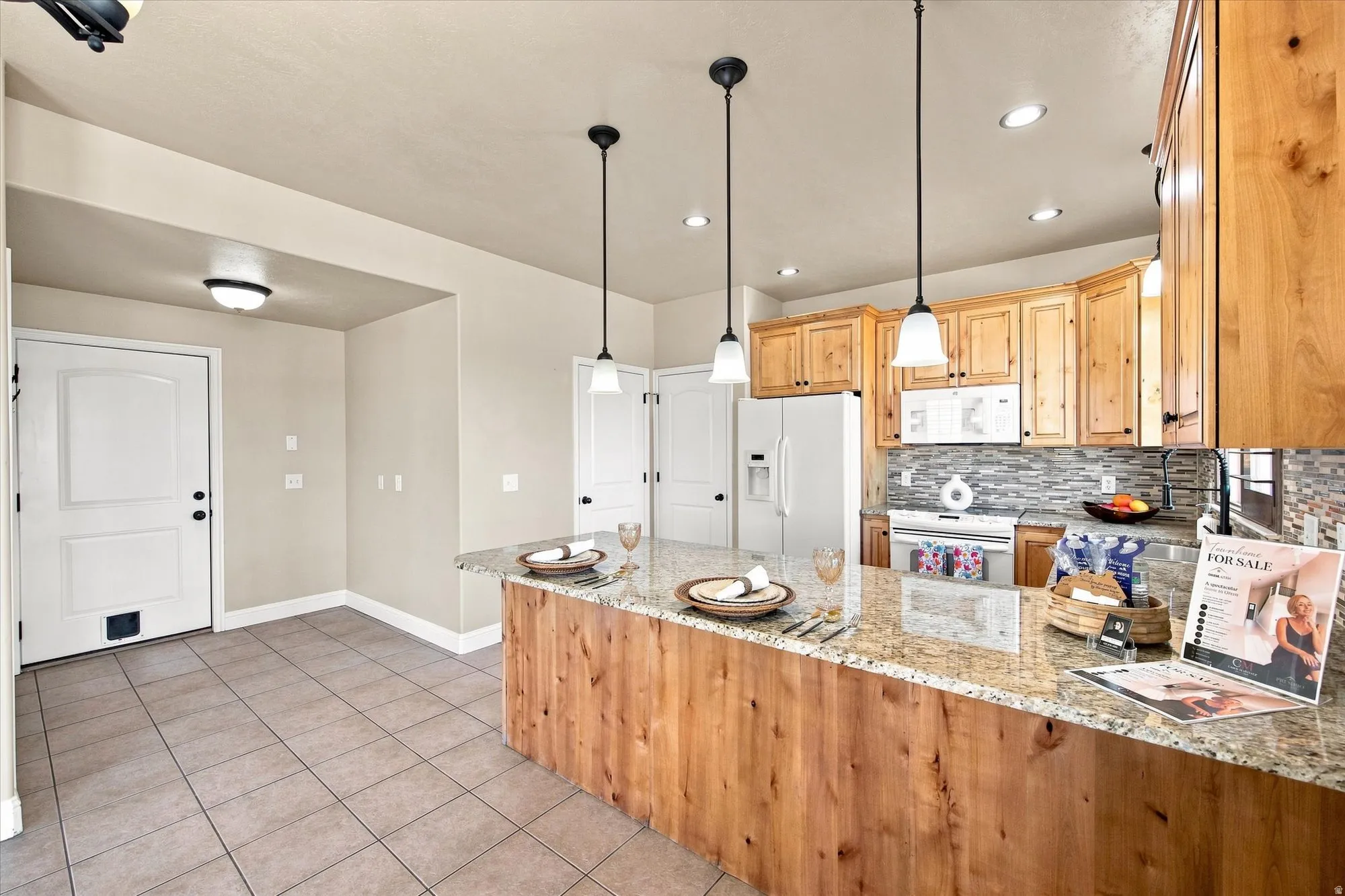 Kitchen featuring wood cabinetry, a granite-finish island with pendant lighting, a tile backsplash, and white appliances