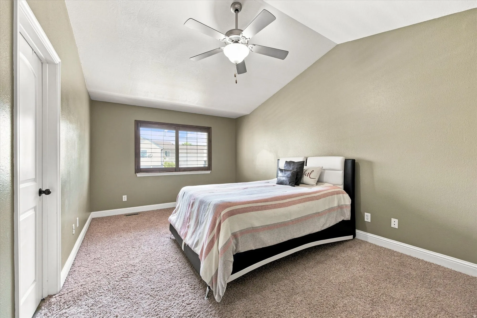 Vaulted ceiling with a ceiling fan, carpeted flooring, and a window with plantation shutters