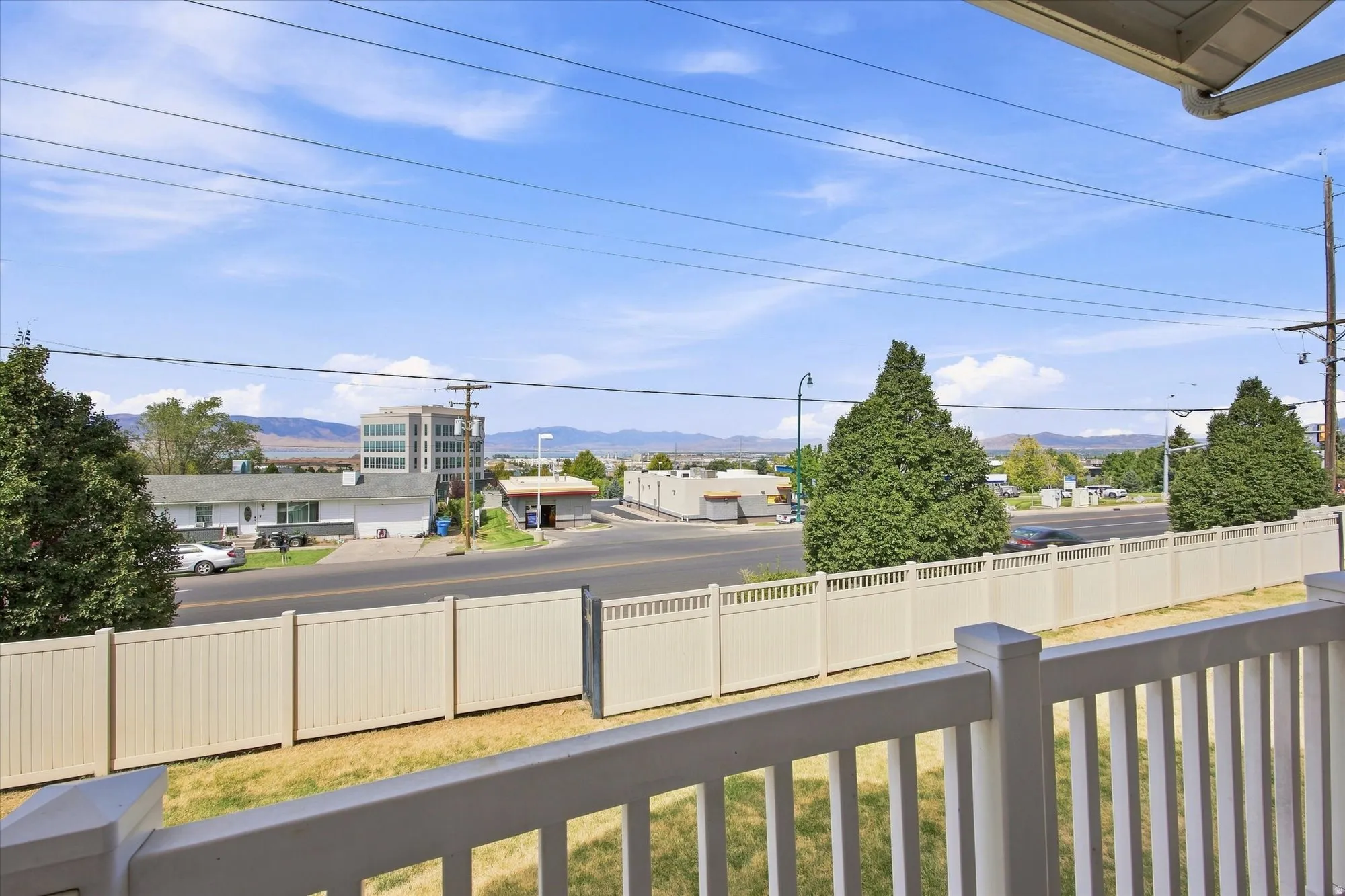 Balcony with white railing, overlooking a street and distant mountains