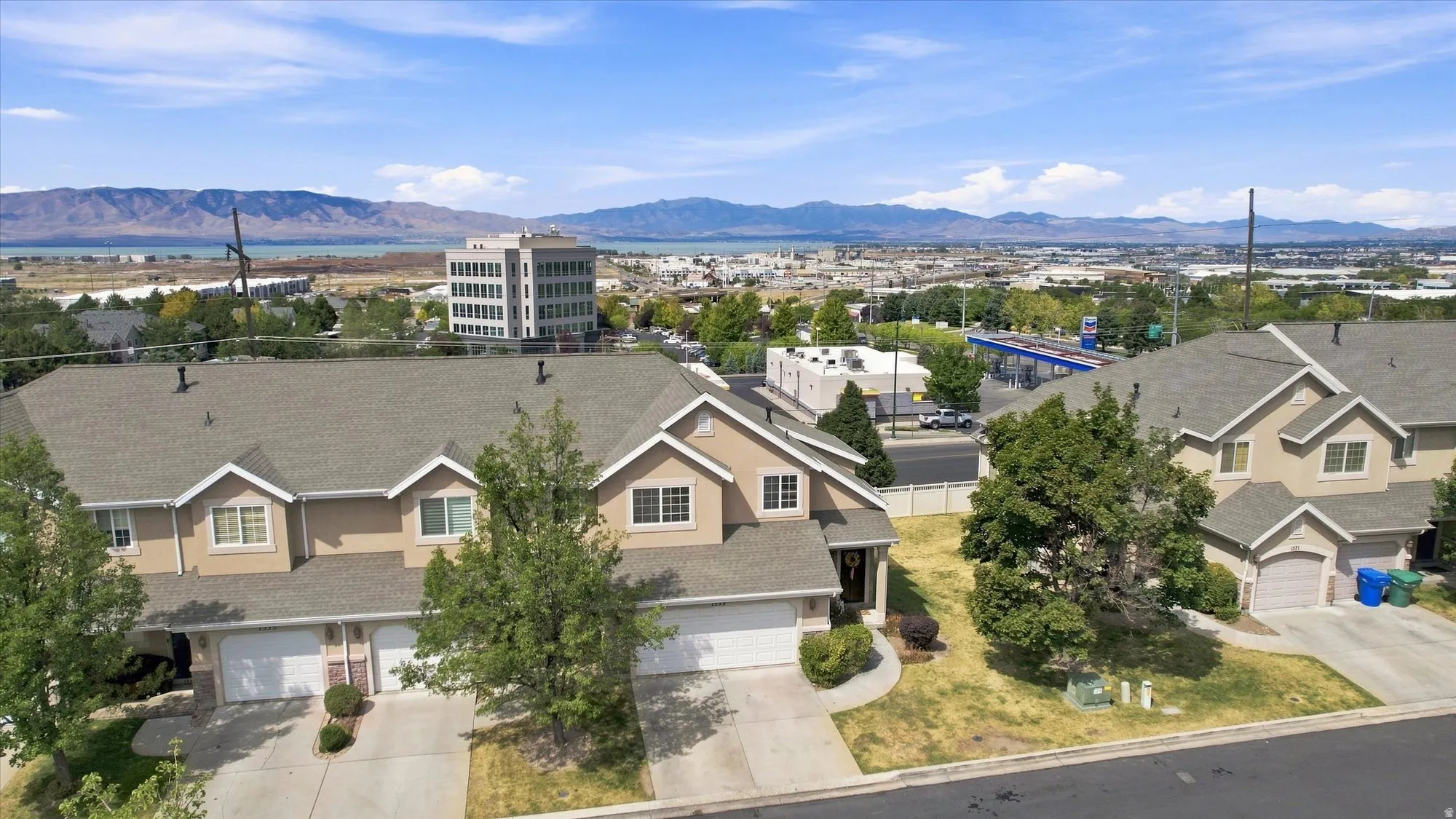 Townhouse-style property featuring a light-colored stucco exterior, attached garages, and a paved driveway