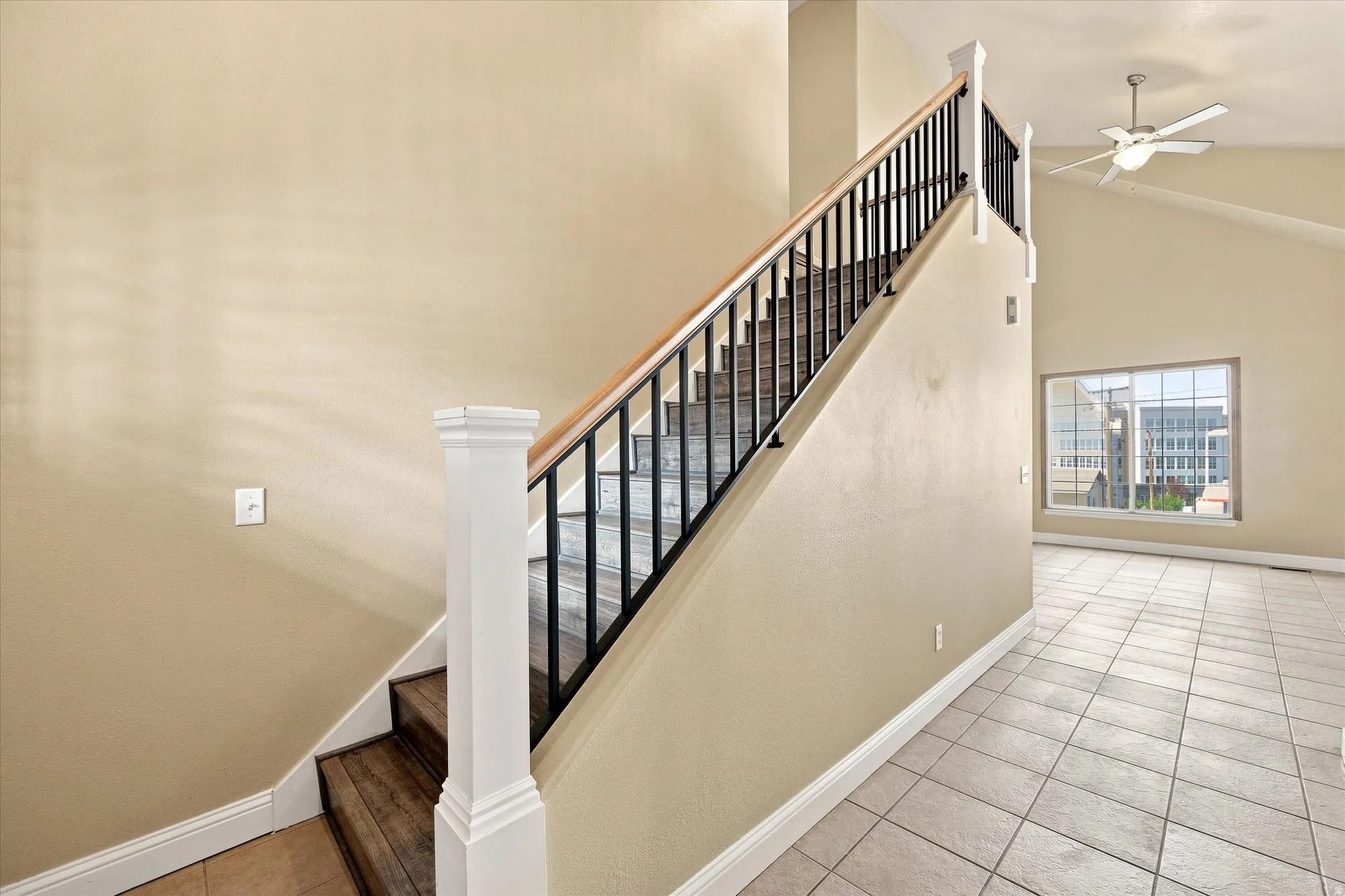 Vaulted ceiling with a ceiling fan, tiled flooring, wood and metal staircase, and a large window