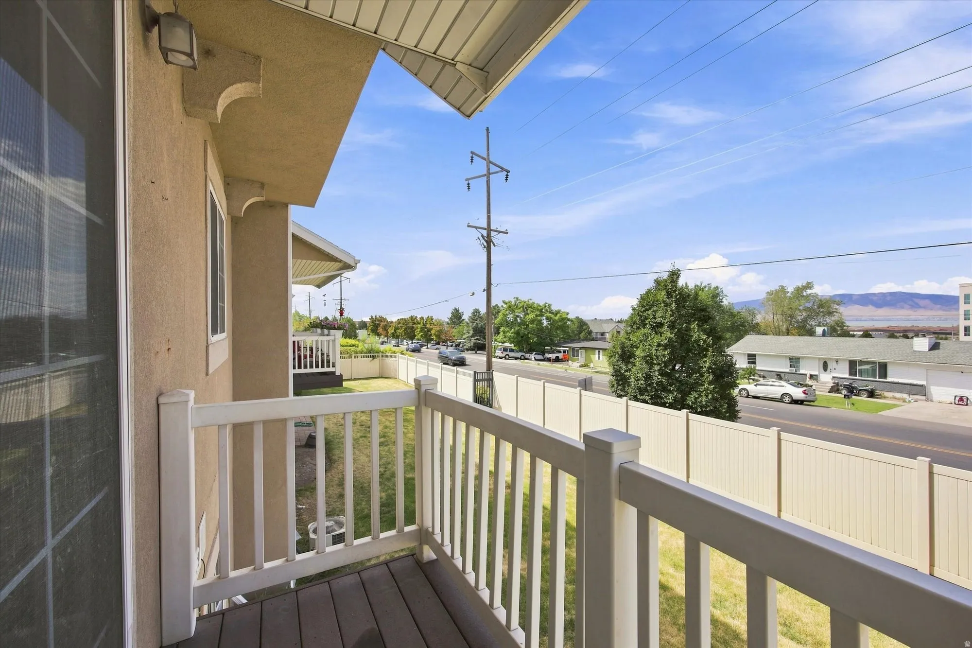 Private balcony with composite decking and white railing, featuring a stucco exterior and exterior lighting
