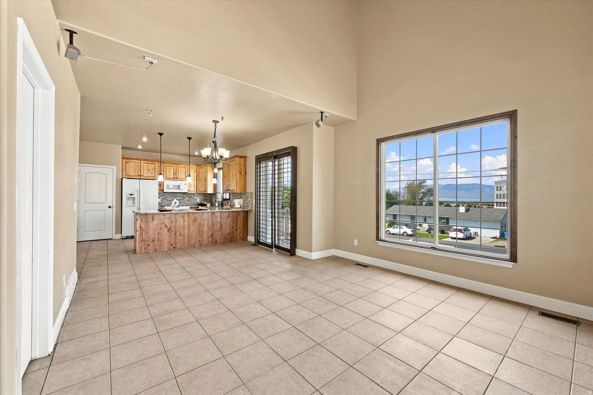 Open-concept living area with vaulted ceilings, large grid-pattern window, tile flooring, and a kitchen featuring wood cabinetry, stainless steel appliances, and a tiled backsplash