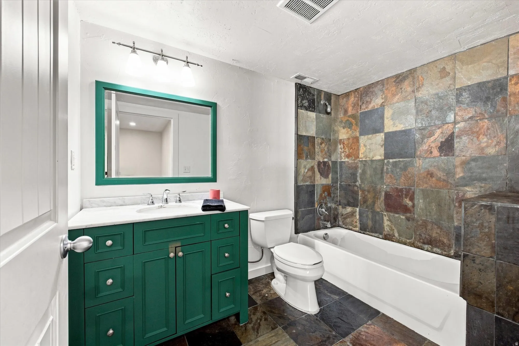 Vanity with a white countertop and integrated sink, green wood-finish cabinetry, a framed mirror, and a wall-mounted light fixture
