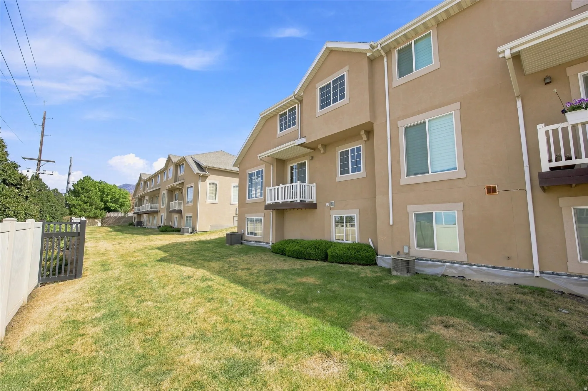Stucco exterior, multiple balconies with white railings, ground-level windows, and a landscaped perimeter