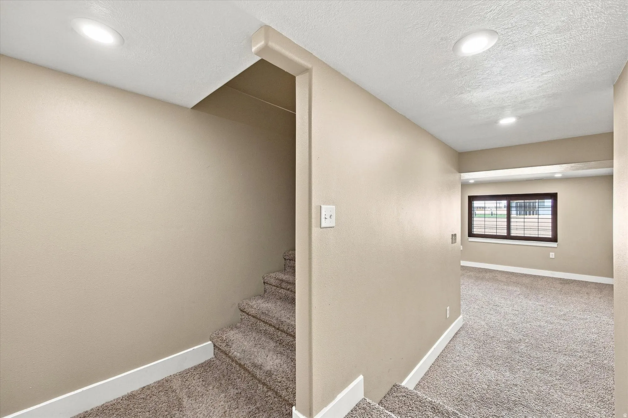 Carpeted stairs leading to a room with a brown-framed window and recessed lighting