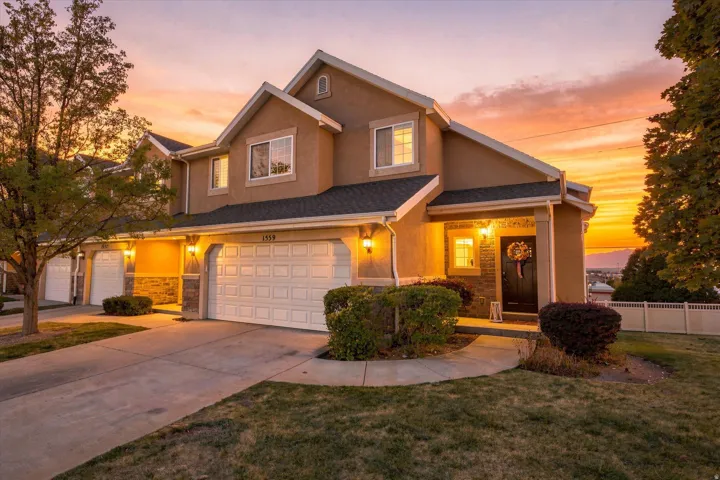 Stucco exterior with stone accents, attached two-car garage, covered front entry, and multiple exterior wall sconces