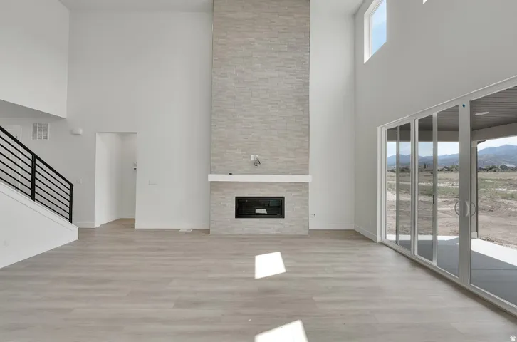 Vaulted ceilings with high windows, light wood-finish flooring, full-height stone-clad fireplace with mantel, and sliding glass doors to outdoor patio