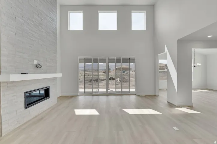 Two-story ceiling, integrated fireplace with a white mantel, floor-to-ceiling textured tile surround, wood-finish flooring, and sliding glass doors
