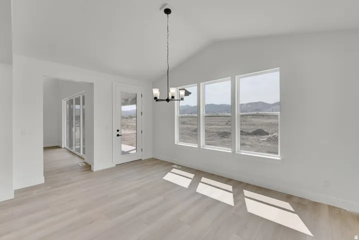 Vaulted ceiling with a contemporary chandelier, multiple windows, wood-finish flooring, and a glass-paneled exterior door