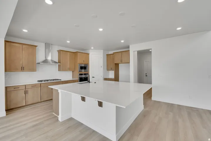 Kitchen featuring a large island, wood-finish cabinetry, stainless steel appliances, white subway tile backsplash, and light wood-finish flooring