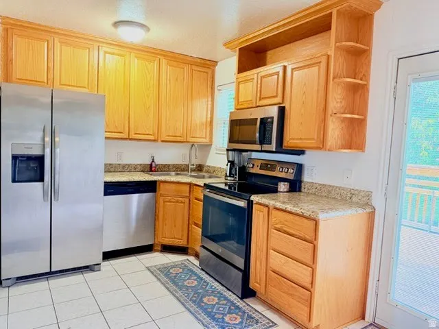 Bright and functional kitchen featuring warm wood cabinetry, stainless steel appliances including a side-by-side refrigerator and electric range, granite countertops, tile flooring, and abundant cabinet storage