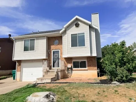 Multi-level exterior with brick and siding facade, integrated garage, concrete steps with wrought iron railing, and a circular window accent
