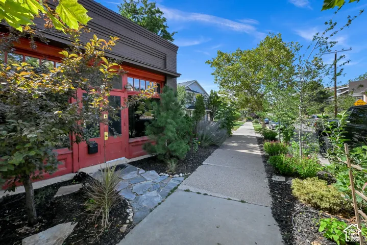 Red entrance door with transom window, extensive landscaping, flagstone pathway, and concrete sidewalk