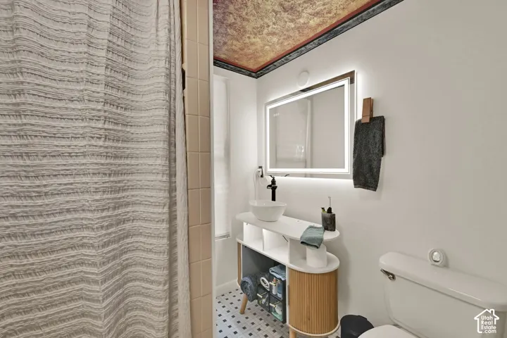 Illuminated vanity mirror, floating vanity with vessel sink, black-finish faucet, and patterned floor tile