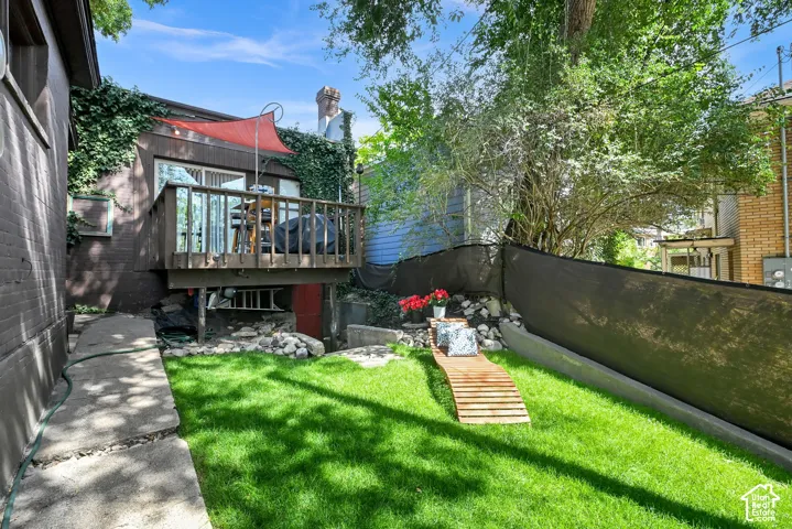 Wood deck with railings, privacy screen, concrete pathway, and lawn area