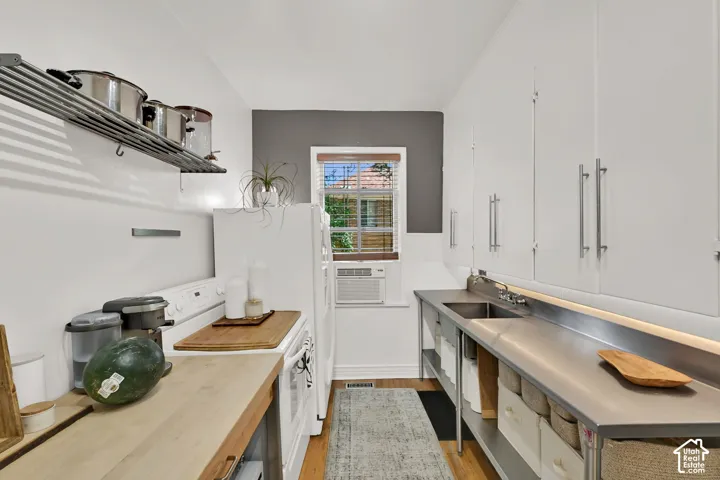 Galley kitchen featuring wood-finish countertops, stainless steel sink, white cabinetry with brushed metal hardware, and a white door with window panes providing natural light