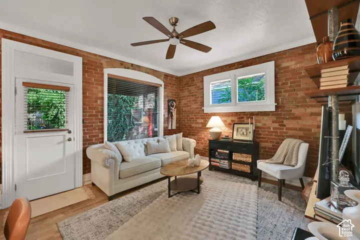Exposed brick accent wall, wood-finish flooring, ceiling fan, white trim, and a white paneled door