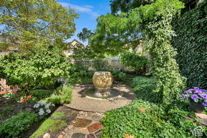 Lush landscaping featuring a stone water fountain, flagstone pathway, gravel circular patio, and mature trees