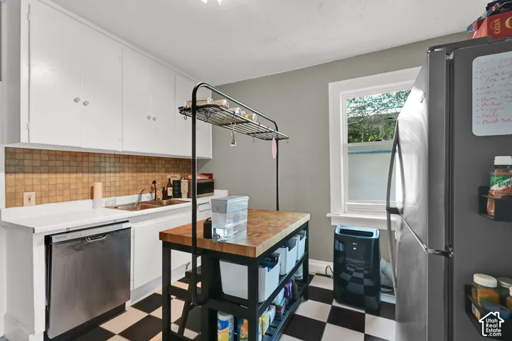 White cabinetry, checkered flooring, stainless steel dishwasher, and a window providing natural light