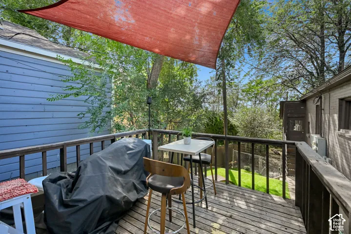Outdoor wood-finish deck with railings, an overhead shade sail, and a view of surrounding greenery