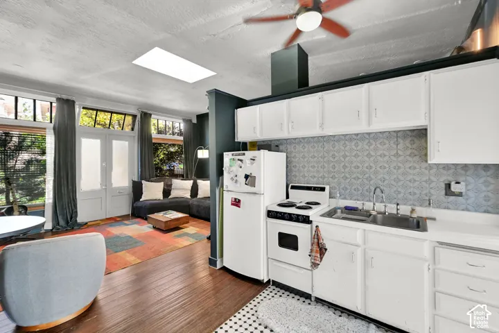 Compact kitchen featuring white cabinetry and appliances, patterned backsplash, and a stainless steel sink